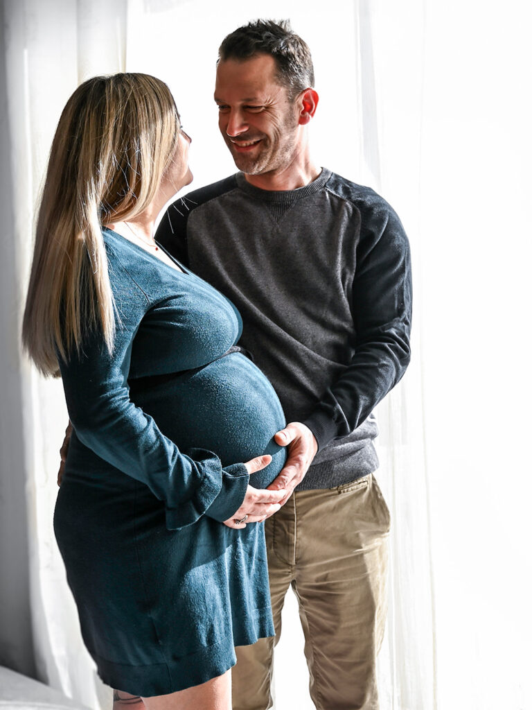 Photo d'un futur papa souriant qui tient le ventre de sa femme enceinte par Simone Photographie