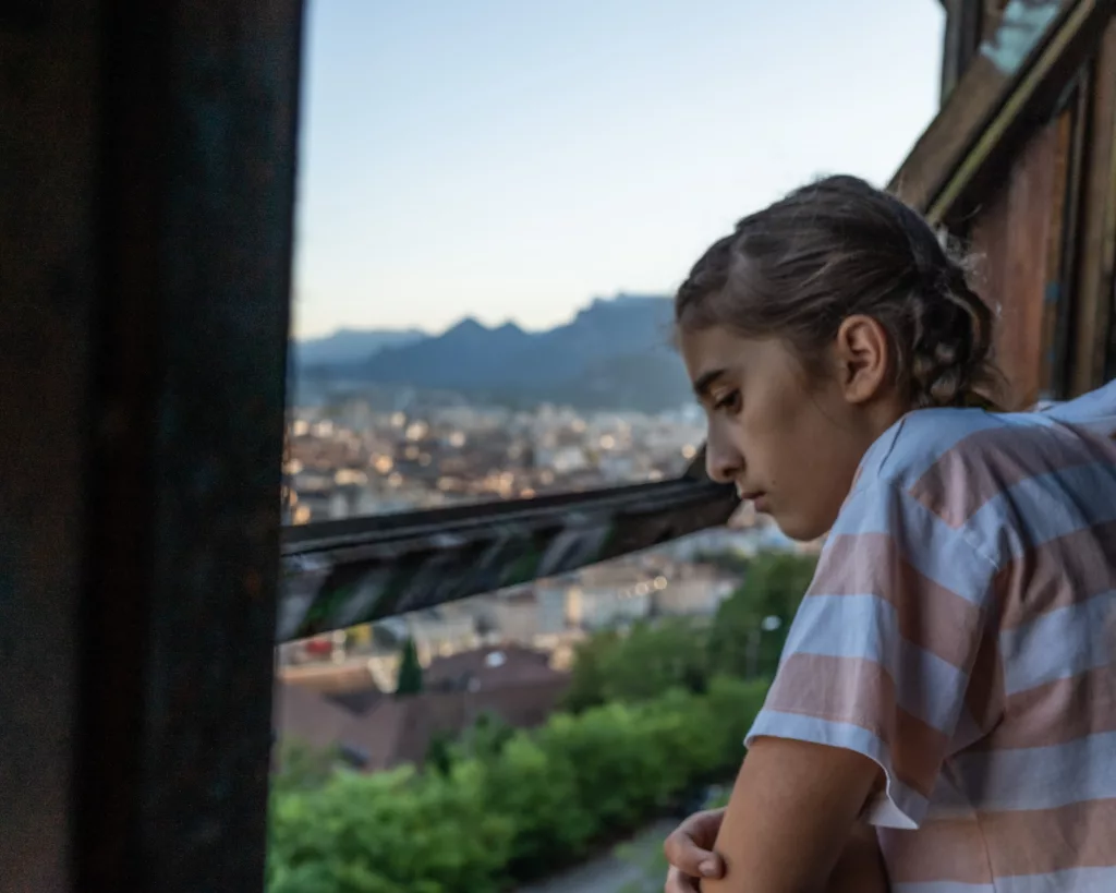 Jeune fille regardant par une fenêtre au dessus de la ville de Grenoble par Simone Photographie