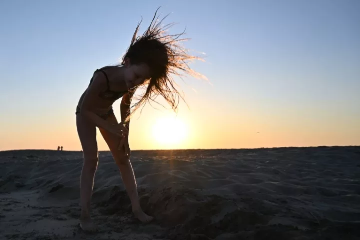 Photo d'une petite fille dans le sable, contre jour avec coucher de soleil